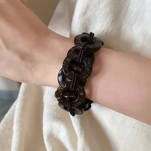 Dettaglio ravvicinato di un bracciale in perle di cocco scure con dischi tondi sul polso