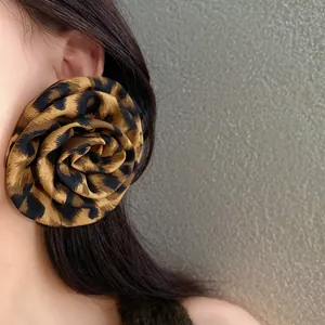 Dettaglio di un grande orecchino a fiore in tessuto leopardato sull'orecchio di una modella.