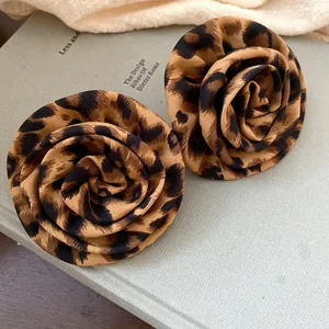 Primo piano di eleganti orecchini in tessuto leopardato a forma di rosa su un libro.