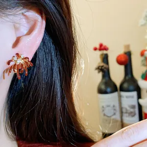 Detailed view of red firework zircon stud earring worn on ear with holiday backdrop