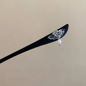 Close-up detail of a wooden hair stick featuring a filigree butterfly and pearl drop