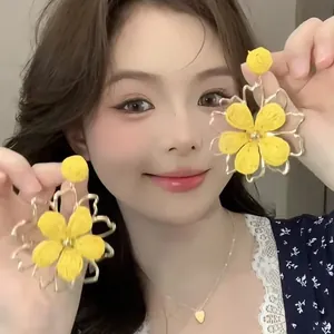 Detailed view of yellow fabric flower earrings with gold metal frame worn by model