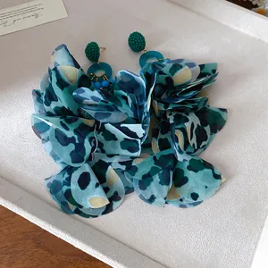 Macro di orecchini a petali in tessuto leopardato verde su vassoio bianco