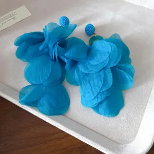 Dettaglio macro di orecchini a petali di tessuto blu vibrante su un vassoio grigio.