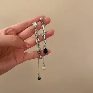 Close-up detail of silver-tone asymmetric long tassel earrings with pearls and black stones