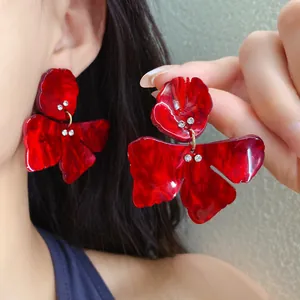 Detailed view of large red resin flower earrings with rhinestones worn by a model