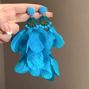 Dettaglio di orecchini a nappa con petali blu e strati di tessuto vivaci per stile spiaggia.