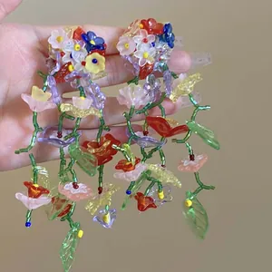 Close-up of handmade colorful glass flower earrings held in hand to show intricate detail.