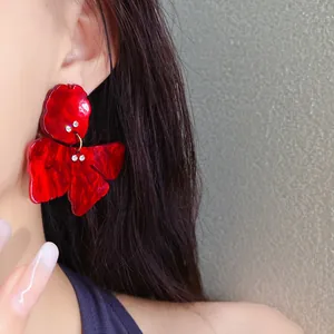 Close-up of elegant red resin flower stud earrings with small rhinestones on an Asian model