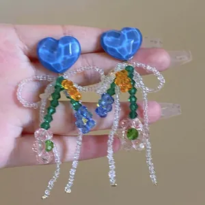 Close-up detail of blue glass heart earrings with colorful beaded floral tassel design