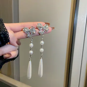 Close-up of sparkling rhinestone bow earrings with elegant long pearl tassels for weddings.