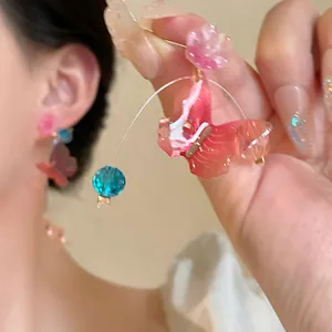Detailed close-up showing pink resin butterfly and blue bead on a silver needle earring