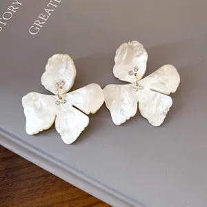 Close-up detail of white resin flower earrings with gold-tone links and clear rhinestones