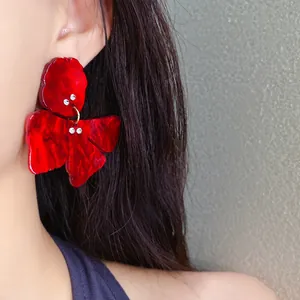 Close-up detail of vintage style red resin flower earrings with small rhinestones on ear