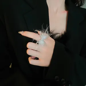 Vista detallada de un elegante anillo abierto con plumas blancas y diseño de mariposa de metal