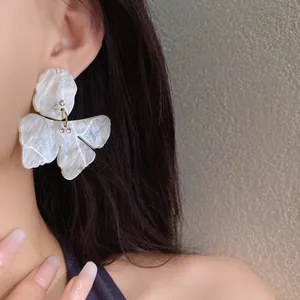 Detailed close-up view of white resin flower earring with rhinestone accents on ear