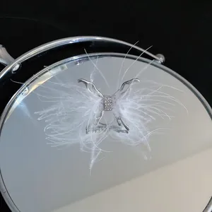 Detalle de anillo de mariposa plateado con plumas blancas y cristales brillantes
