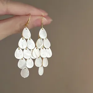Detailed macro shot of elegant tiered white teardrop shell drop earrings in gold finish.