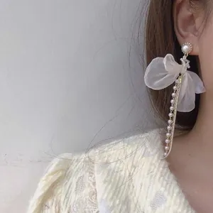 Detalle de un pendiente elegante con lazo de organza blanca y perlas en una modelo.