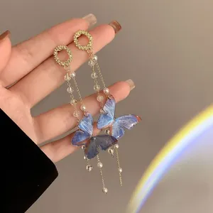 Primer plano detallado de pendientes de mariposa azul con perlas y borlas largas.