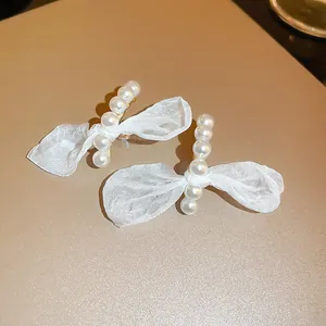 Primer plano de elegantes pendientes con lazo, perlas blancas y tejido de encaje
