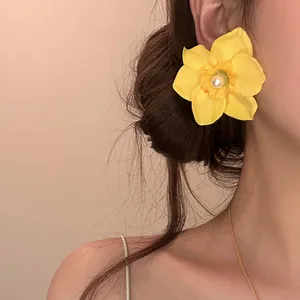 Primer plano de un pendiente de flor amarilla con perla lucido por una modelo joven