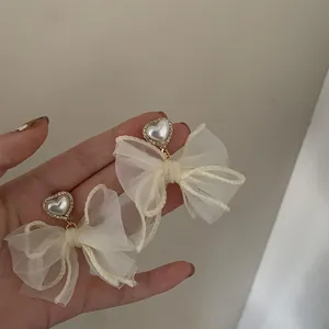 Detalle de los pendientes de lazo de malla crema con perlas de corazón y pedrería.