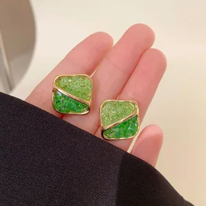 Macro view of square gold-rimmed stud earrings inlaid with vibrant green crushed crystals