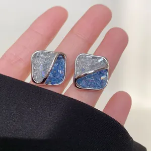 Detailed macro shot of silver square stud earrings with blue and clear crushed crystal