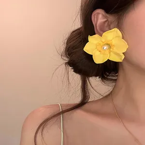 Primer plano de un pendiente de orquídea amarilla con perla usado por una modelo