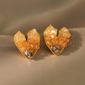 Macro view of luxury heart-shaped stud earrings featuring clustered amber crystals on gold base