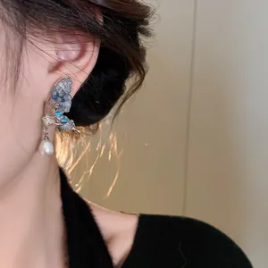 Close-up detail shot of a silver butterfly earring with crystal inlay and pearl on an ear.