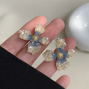 Detailed view of fashionable blue and beige crystal flower stud earrings on fingers.