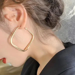 Close-up of large gold geometric square hoop earring worn by a model