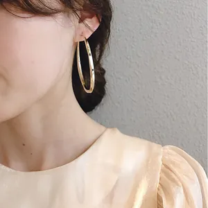 Detailed view of an exaggerated large gold metal hoop earring worn by a model in satin dress