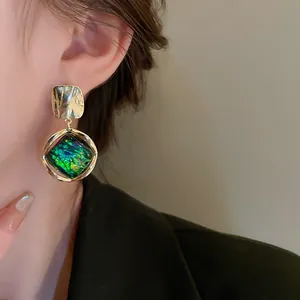 Primer plano de elegantes pendientes geométricos vintage con piedra verde y acabado dorado