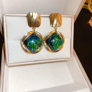 Primer plano de pendientes geométricos vintage con resina veteada verde y dorada