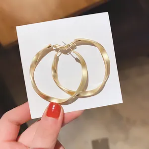 Close-up detail of matte gold twisted geometric metal hoop earrings on a display card