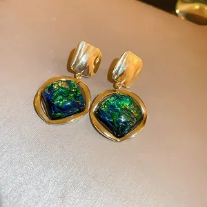 Primer plano detallado de pendientes vintage de oro con piedras cuadradas verdes irisadas.