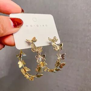 Detailed close-up view of elegant gold-colored butterfly hoop earrings on a white display card