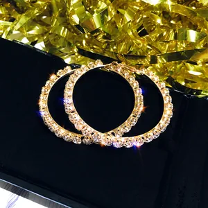 Close-up of sparkling oversized crystal-encrusted gold hoop earrings on black velvet.