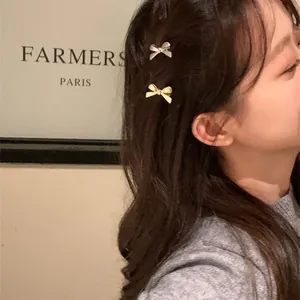 Détail de deux mini barrettes à cheveux en forme de nœud métallique sur une frange.