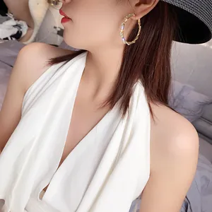 Close-up of a model wearing large twisted gold hoop earrings with sparkling rhinestones