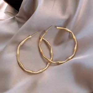Close-up of oversized gold-tone bamboo joint textured hoop earrings on satin