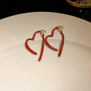 Minimalist red enamel heart-shaped gold plated stud earrings presented on an elegant beige plate