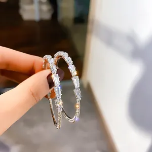 Close-up detail of silver hoop earrings with rectangular and round sparkling crystals
