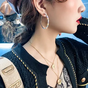 Close-up of model wearing large rhinestone-studded silver hoop earrings and coin necklace.