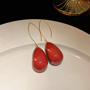 Close-up of elegant red teardrop drop earrings with gold hooks on a white plate