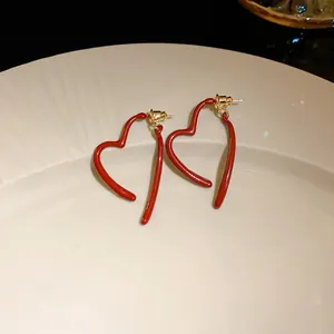 Detailed view of red glossy heart-shaped stud earrings on a cream ceramic plate