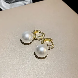 Macro detail of elegant gold-plated hoop earrings featuring pavé zircons and white pearls